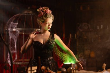 Cadılar Bayramı cadısı ve kazan. Büyücülük yapan genç ve güzel bir kadın. Ürkütücü zindan karanlık odası. Büyücü kadın aşk iksiri hazırla. Sihir kullan.