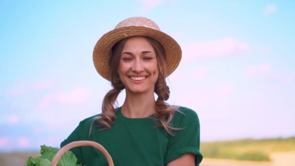 農地に立っている野菜でいっぱいのバスケットを持っているわら帽子の女性農家 笑顔の女性アグロニスト専門農業農業アグリビジネスカメラ — ストック動画