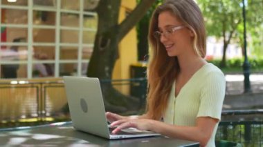 Caddedeki kafede dizüstü bilgisayarda yazan mutlu kadın blogcu. Moda gözlüklü, kendine güvenen genç bir kadın açık kafe terasında yeni blog için netbook 'a yazı yazıyor. Blogcu blog yazmak için açık havada yazıyor.
