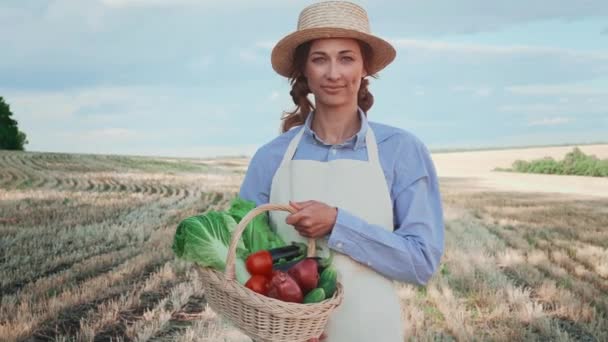 女农民头戴草帽 提着装满蔬菜的篮子站在农田里 农艺学界微笑的女性专家的画像 穿围裙的漂亮姑娘 — 图库视频影像