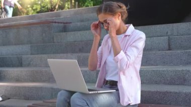 İş kadını parkta dizüstü bilgisayar kullanarak merdivenlerde oturuyor. Gözlük takıp uzaktan çalışan mutlu bir genç serbest yazar. Gülümseyen Kafkasyalı kadın video çağrı çalışmasını online ders haline getirdi.