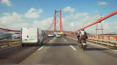 Portekiz, Lizbon 03 Mart 2024 'te 25 de Abril Köprüsü' nde güneşli yaz gününde Lizbon, Portekiz 'de bulutlu mavi gökyüzünün altında hareket eden trafiğin hızlandırılmış görüntüsü.