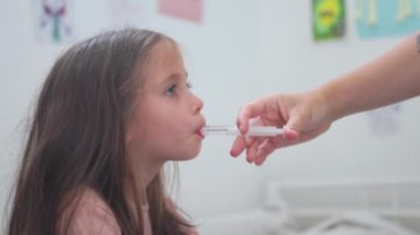 İlgili bir anne kızına şırıngayla ilaç veriyor. Annenin eli, soğukta küçük bir kızın ağzına bakteriyel enfeksiyonla birlikte antibiyotik enjekte ediyor..