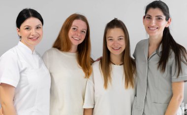 Üniformalı kozmetologların grup portresi bir arada duruyor ve kameraya bakıyor. Güzellik kliniğinde kameraya gülümseyen kadın dermatologlar..