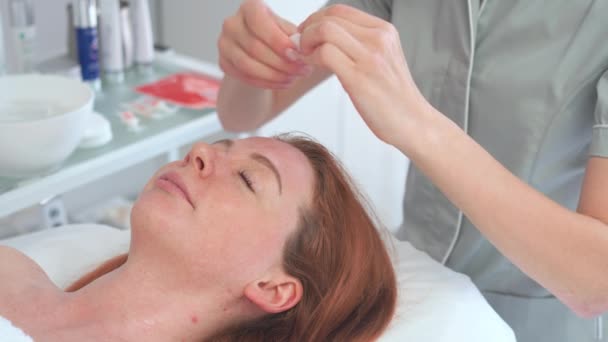 フェイススキンケア 美容院で血清オイル治療を受けている美しい女性 センターの顧客の頭部に化粧品血清を適用する化粧品学者 — ストック動画