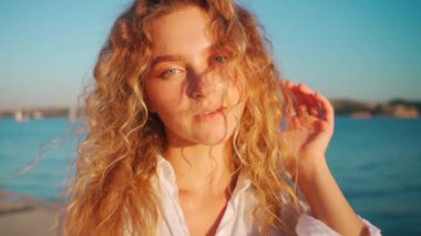 Uzun sarı dalgalı saçlı, duygusal bir kadın. Kameraya bakan beyaz gömlekli çekici bir kadın portresi. Kendine güvenen bir kadın mavi gökyüzünün altında, nehrin kenarında duruyor..