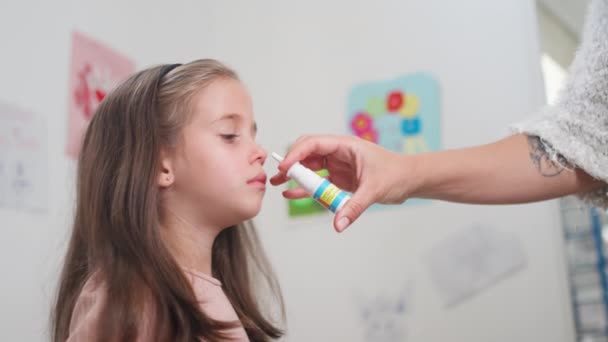 病気の娘の鼻に鼻スプレーを噴霧する母親の世話 自宅で鼻の薬を使用して小さな病気の少女を治療する女性の作物手 — ストック動画