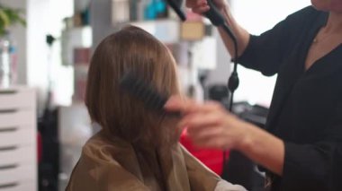 Çok tatlı bir kız berber dükkanında saç kurutma makinesi ve kadın kuaförle saç şekillendiriyor. Kadın çocuk, isimsiz bir berberden yeni bir saç stili alıyor..