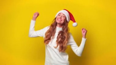 Noel Baba şapkalı neşeli kadın parlak sarı arka planda dans ediyor. Genç beyaz kadın Noel boyunca arka planda kutlama yapıyor..