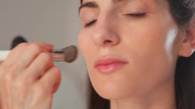 Makyaj sanatçısı stüdyoda kadınların yüzüne fondöten yapıyor. Güzel genç bayan model profesyonel stilist tarafından foto çekimine hazırlanıyor.. 