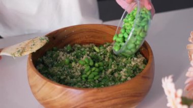 İsimsiz kadın elleri, ahşap kasedeki yeşil salataya taze edamame fasulyesi ekliyor. Kadın evde mutfakta öğle yemeği için lezzetli sağlıklı yemekler hazırlıyor..