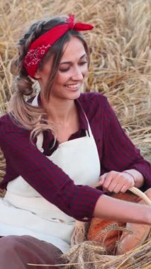 Gülümseyen kadın çiftçi buğday tarlasında oturuyor. Hasır sepetli eko ürünü olan bir kadın fırıncı. Önlüklü, beyaz bir kadın. Organik sağlıklı gıda konsepti.