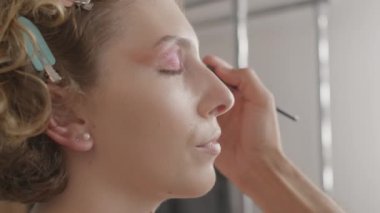 Profesyonel makyöz elleri stüdyoda fırçayla kadın modele makyaj yapıyor. Mutlu kadın stüdyoda fotoğraf çekimine hazırlanırken kameraya bakıyor.. 