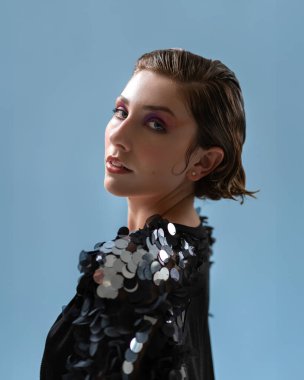 Makyajlı ve zarif pullu ceketli güzel bir model portresi. Çekici bir kadının, mavi arka planda kamera karşısına geçişini gösteren bir çekim..