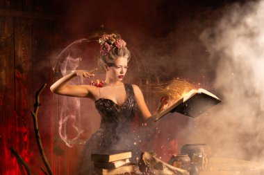 Eski şatoda elinde büyüler kitabı tutan, antika siyah bir elbise giymiş çekici genç bir kadın. Cadılar Bayramı kutlaması, cadılık konsepti, peri masalı atmosferi. Sihirbazlık büyüleri.