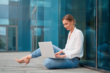 Modern ofisin dışında dizüstü bilgisayar kullanan genç bir iş kadınının tüm vücudu. Cam inşaatına karşı netbook üzerinde çalışan akıllı, kendine güvenen kadın girişimci..