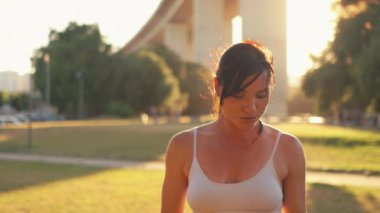 Spor sutyeniyle koşan, bacak kaslarını esneten, parkta çimlerin üzerinde oturan bir kadın. Bayan koşucu dışarıda oturarak esneme egzersizleri yapıyor. Spor kadını güneşli bir günde sahada geriniyor..