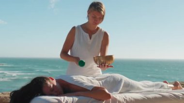 Kadın rahatlatıcı masaj yapıyor, meditasyon yapıyor, okyanus kenarında Tibet müzik sesiyle terapi yapıyor. Stres atmak. Ses terapisi, dinlenme, meditasyon, sağlıklı yaşam tarzı..
