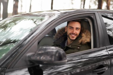 Beyaz adam güneşli kış gününde arabasında oturuyor. Kış tatili. Mutlu gülümseyen hippi adam arabada oturuyor ve pencereye bakıyor. Portre Pozitif sürücü