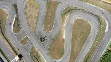 Birkaç kartın dolambaçlı pistte yarıştığı go-kart pistinin hava aracı görüntüsü. Dinamik sahne yukarıdan kart yarışlarının hızını ve heyecanını yakalıyor