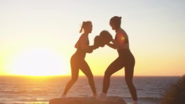 Parlak günbatımında plajda deniz manzarası ve gökyüzü manzaralı kayalarda boks antrenmanı yapan sırt ışıklandırmalı kadın boksörler. Kararlı genç kadın boksörler, doğada kutlama yaparken beşlik çakıyor.. 