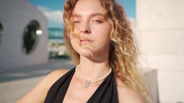 Güneşli bir günde gülümseyen kıvırcık sarı saçlı güzel bir genç kadının yakın çekimi. Duyarlı dişi dışarı bakıyor.. 