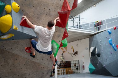 Spor salonunda dağa tırmanmaya kararlı bir adam. Yetişkin bir adamın spor merkezinde kayalık çalışması güvenlik ipi olmadan renkli yapay duvara tırmanması..