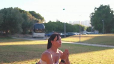 Güneşli bir günde şehir parkında zıplama egzersizi yapmaya kararlı bir kadın. Gündüz vakti çimenlikte spor giyinen genç ve fit bir kadın.. 