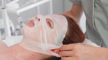 Masör kozmetoloji salonundaki kadına yüz maskesi takıyor. Sakin bayan müşteri güzellik merkezinde isimsiz bir güzellik uzmanı tarafından şımartılıyor.. 