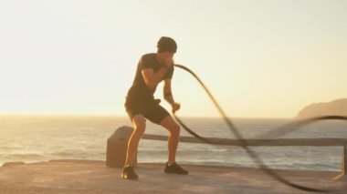 Atletik erkek fitness modeli gün batımında denize karşı savaş ipi eğitimi. Spor fitness sağlıklı yaşam tarzı konsepti. Beyaz tenli, kaslı vücut fonksiyonel eğitim dayanıklılığı.