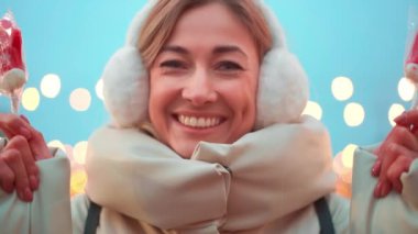 Mutlu kadın Noel pazarında eldiven şeklinde şekerler tutuyor. Gülümseyen beyaz kadın festival sezonunda kışın kuklalar takıyor ve boynunu ısıtıyor.. 