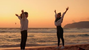 Dişi arkadaşlar gün batımında sahilde ısınma egzersizleri yapıyorlar. Spor giyinen kadınlar doğada birlikte spor yapıyorlar.. 