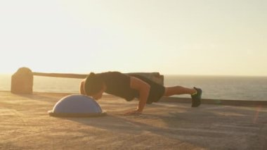 Spor giyim sektöründe yarı dengeli antrenör kullanarak şınav çeken kararlı bir sporcu. Gün batımında gökyüzü altında spor yapan genç bir adam. Fitness ve sağlıklı yaşam tarzı.