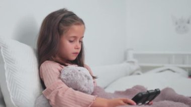 Hasta kız evde yatakta battaniyeyle otururken dijital tablet kullanıyor. Yatakta dinlenirken portatif cihaz kullanırken gözünü kaçırıyor.. 