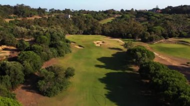 Drone, güneşli bir günde yemyeşil ağaçlarla çevrili golf sahasının nefes kesici manzarasını yakalar. Huzurlu ve pitoresk bir manzara yaratır. 