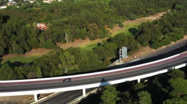 Hava görüntüsü, yoğun, yemyeşil ağaçlarla çevrili köprüden geçen arabaları yakalıyor. Yol, insan yapımı yapıyı ve canlı yeşilliği gözler önüne sererek doğal manzarayı kesiyor. 