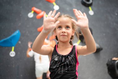 Güzel, sevimli dağcı kız ellerini toz tebeşirle kaplamış magnezyumla gösteriyor. Spor merkezinde kaya tırmanışına hazırlanan kararlı bir çocuk. Fitness ve sağlıklı yaşam tarzı.