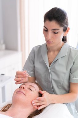 Yüz bakımı. Güzeller güzeli kadın güzellik salonunda serum yağı tedavisi görüyor. Kozmetik uzmanı merkezdeki müşteri şefine kozmetik serumu uyguluyor..