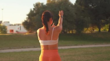 Parlak güneşli bir günde şehir parkında kol egzersizi yapan formda bir kadın. Kararlı genç dişi gündüz egzersizleri yaparken ellerini kaldırıyor.. 