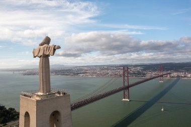 Kral heykeli, kollarını açmış, Lizbon 'daki Tagus Nehri' nin sakin sularına bakan 25 de Abril Köprüsü 'ne bakan gökyüzü bulutlu, gökyüzü manzaralı İsa heykeli dimdik ayakta duruyor.
