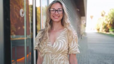 Kahverengi elbiseli ve uzun sarı saçlı gözlüklü şık bir kadın kafenin kapısından çıkıyor ve kafe boyunca kameraya gülümserken yürüyor. Şehir cazibesini ve kişisel tarzını gösteriyor