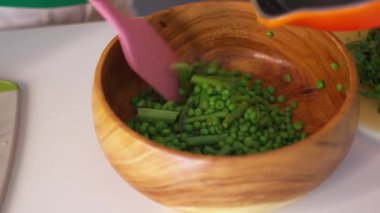 Tanınmayan kadın elleri taze kuşkonmaz ve ahşap kaseye yeşil bezelye döküyor. Kadınlar mutfakta öğle yemeği için lezzetli yeşil salata hazırlıyorlar.. 
