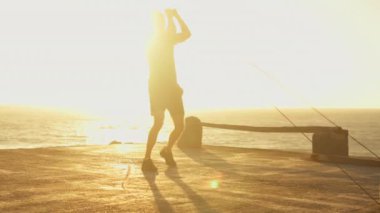 Aktif erkek atlet gün batımında iskelede elastik direniş bandıyla güç antrenmanı yapıyor. Aktif giyimde kararlı sporcu dışarıda sağlıklı yaşam tarzı egzersizi yapıyor..