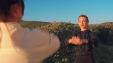 Güneşli bir günde kumlu sahilde kollarını açan sportif kadınlar. Aktif giyimde kararlı bayan arkadaşlar doğada birlikte egzersiz yapıyorlar.. 