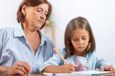 Büyükannem evde renkli kalemle resim çizerken kızı izliyor. Sahne, çocuk yaratıcı aktiviteleriyle uğraşırken cesaret ve hayranlık anlarını yakalıyor. 