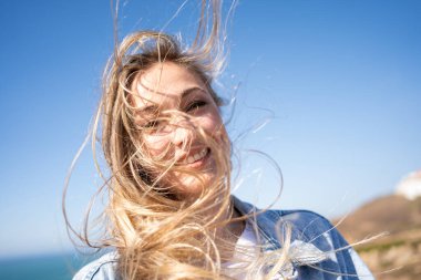 Kumsalda açık mavi gökyüzüne karşı uzun sarı saçları olan gülümseyen kadın. Mutlu güzel bir kadının portresi yaz tatilinde kameraya bakıyor.. 