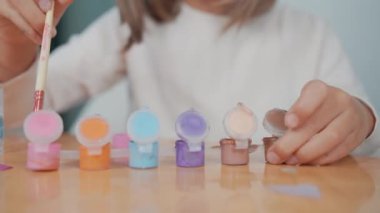 Genç bir kız, iş yerinde yeni renkler yaratmak için renklerin içine fırçalarken canlı resimlerin yakın plan görüntüsü. 