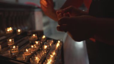Kadın ellerinin mum yakıp Avrupa 'daki Katolik kilisesinde sunağa koyduğu yakın plan. Loş, sakin ortam huzur ve gizemli bir atmosfer yaratıyor, bağlılığı ve inancı vurguluyor.