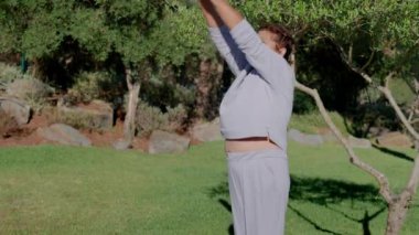 Yaşlı bir dişi, barışçıl bir parkta hafif bir esneme hareketi yapar, esnekliği ve refahı teşvik eder. Bereketli ortam, sabah egzersizinin ferahlatıcı deneyimine katkı sağlar..