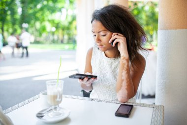 Vitiligo deri bozukluğu olan bir kadın kaldırım kafesinde otururken akıllı telefon kullanıyor. Siyah genç bayan, güneşli bir günde hafta sonu boyunca cihazla mesaj atıyor.. 